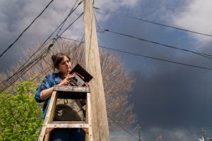 woman on ladder installing small air pollution monitor on telephone poll